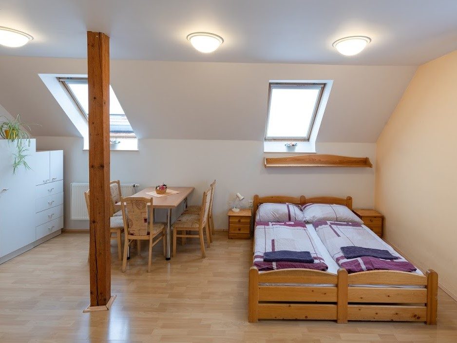 Pokoj s dvěma postelemi a střešními okny, vybavený stolkem se židlemi pro pohodlné posezení.